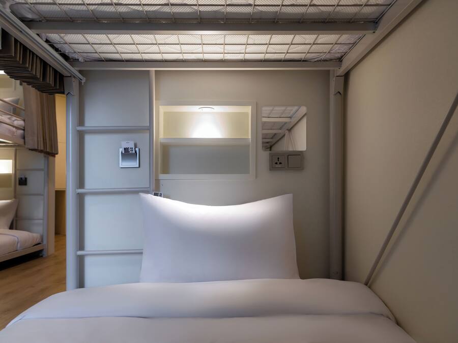 Una habitación de hotel con literas, una mesita de noche, una lámpara de pared y un espejo.
