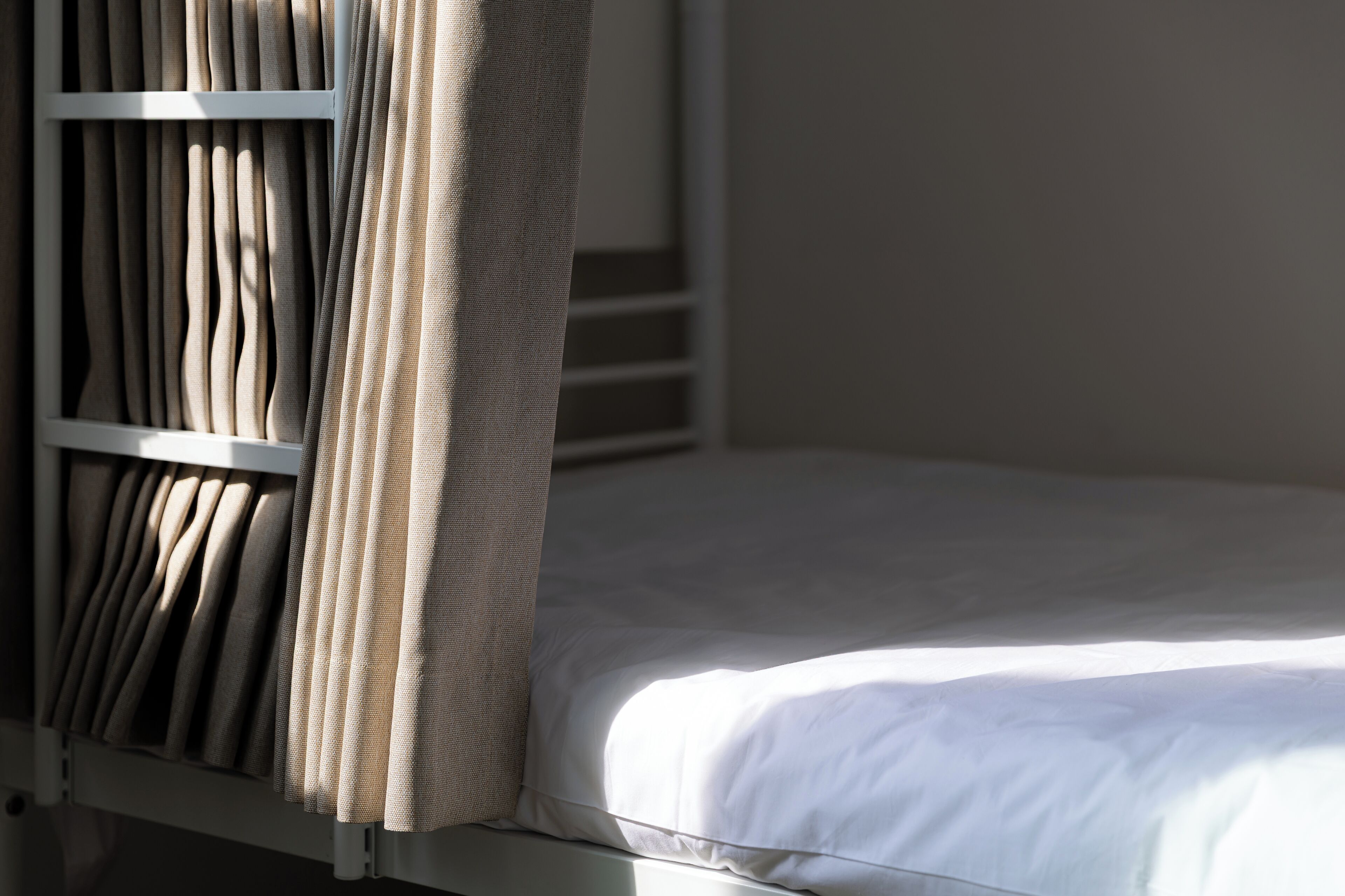 Una cama litera con colchón blanco y cortinas color beige.