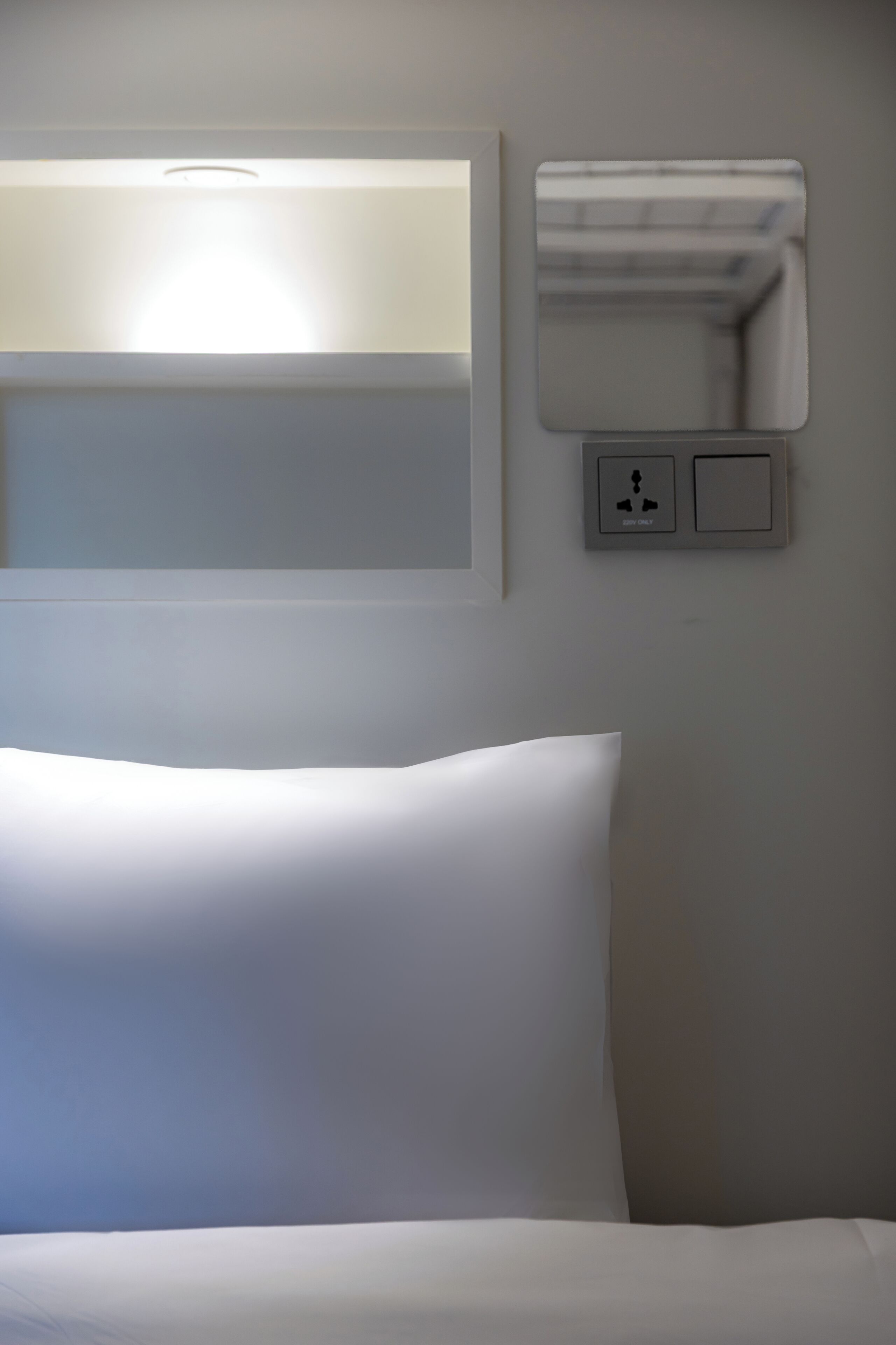 Une chambre d’hôtel équipée d’un lit, d’une lampe fixée au mur et d’un panneau de commande avec un bouton d’alimentation et une icône représentant un haut-parleur.