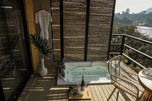 A balcony with a hot tub, a table with glasses and a bottle, and a wicker chair. - La Pausa Hotelbistro (San Luis)