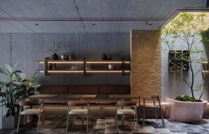 Un intérieur moderne avec un espace salon central, des étagères ornées d’objets décoratifs et un grand pot contenant un arbre.