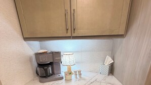 Een kleine keuken met een koffiezetapparaat, een lamp en een pak tissues op het aanrecht.
