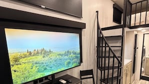 Een modern interieur met een flatscreen televisie aan de wand, een bureau met stoel, een trap en een keukenhoek.