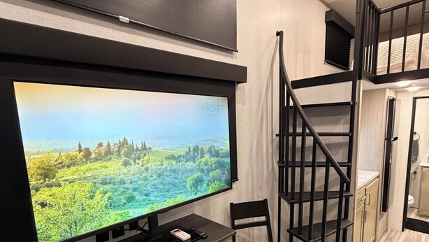 Un interior modern amb un televisor de pantalla plana penjat a la paret, un escriptori amb una cadira, una escala i una zona de cuina.