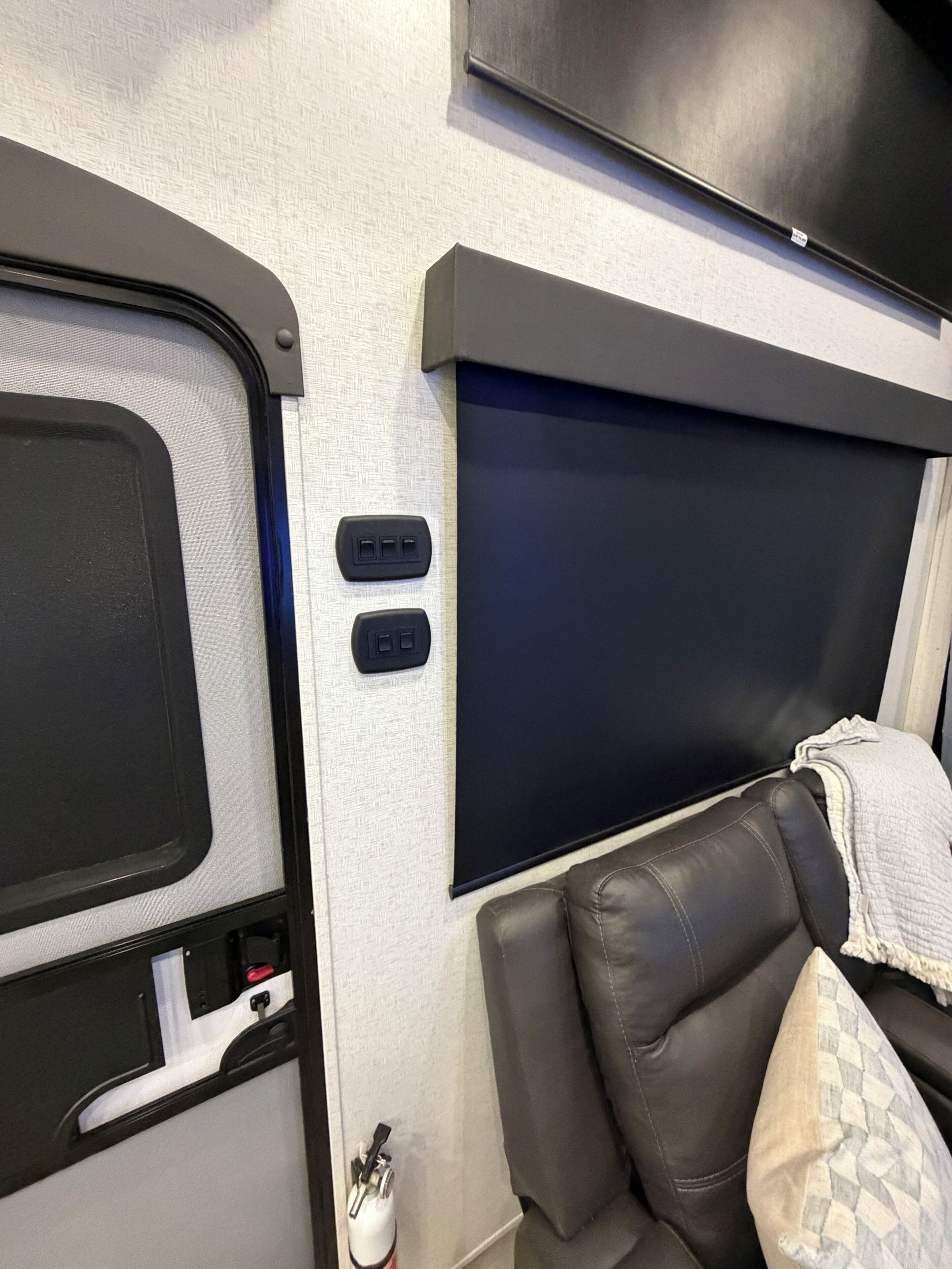 Un espace de vie compact comprenant un lit, un téléviseur fixé au-dessus, et un petit coin salon avec un coussin.