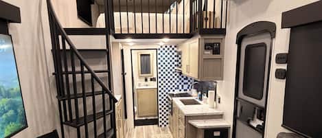 A compact living space with a kitchenette, a dining area, a sofa with a pillow, a small rug, and a staircase.