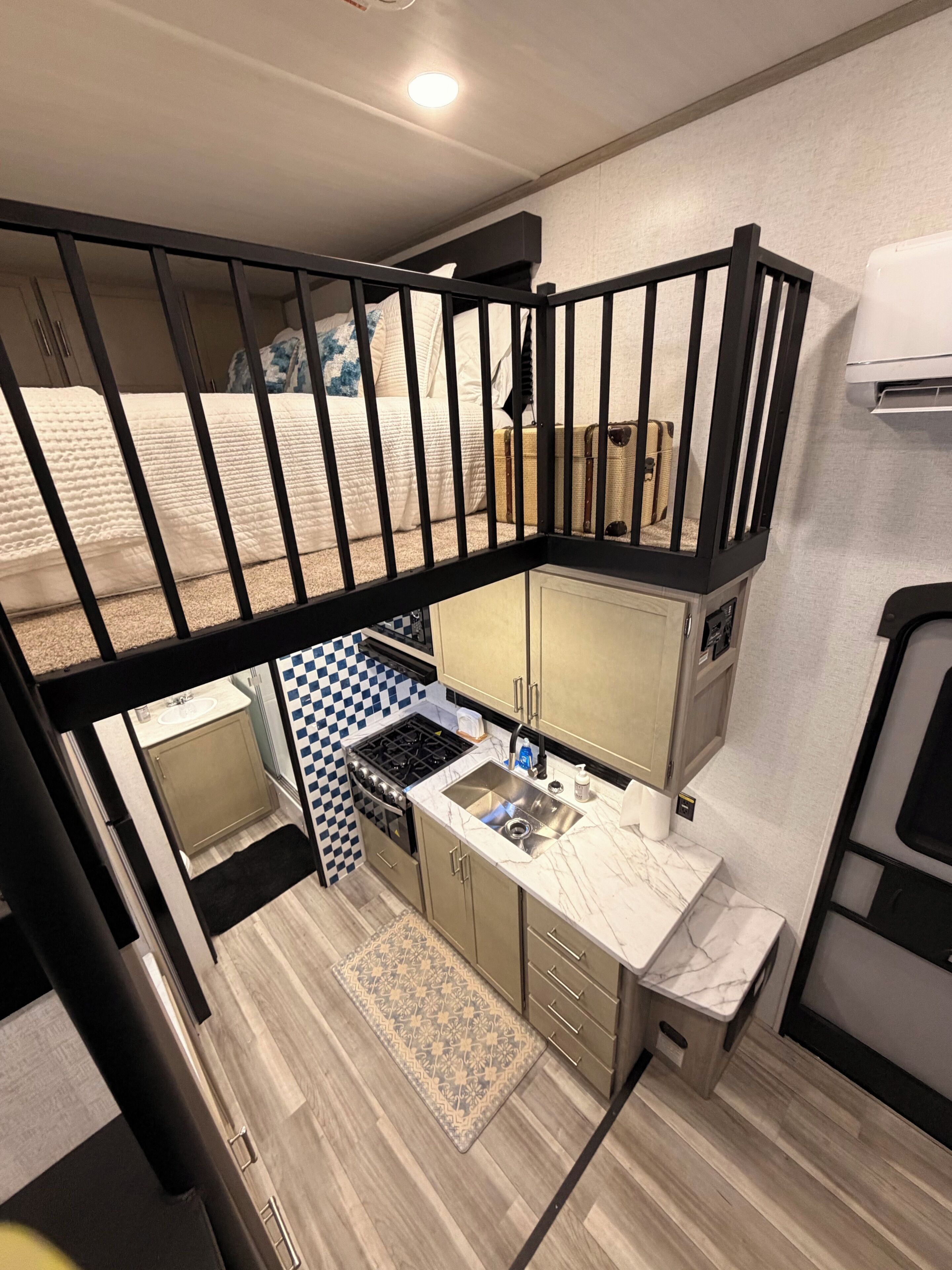 A compact kitchen with a stove, sink, and upper bunk bed.