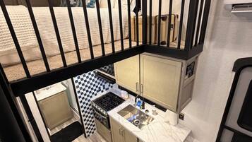 A compact kitchen with a stove, sink, and upper bunk bed.
