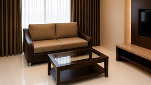 A modern living room with a sofa, a glass-top coffee table, and a flat-screen TV mounted on the wall. - The Regaal - 5 mins from Railway Station (Jalgaon)