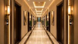 A hotel corridor with numbered doors, wall-mounted light fixtures, and potted plants. - The Regaal - 5 mins from Railway Station (Jalgaon)