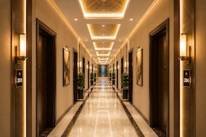 A hotel corridor with numbered doors, wall-mounted light fixtures, and potted plants. - The Regaal - 5 mins from Railway Station (Jalgaon)