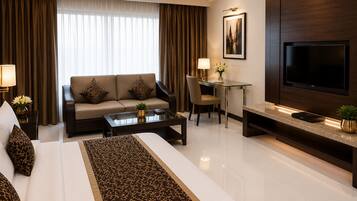 Habitación de hotel moderna con sofá, mesa de comedor, televisor y cama con un corredor estampado.