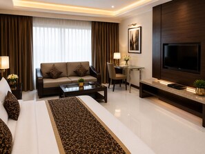 Ein modernes Hotelzimmer mit einer Couch, einem Esstisch, einem Fernseher und einem Bett mit einem gemusterten Laufflächenteppich.