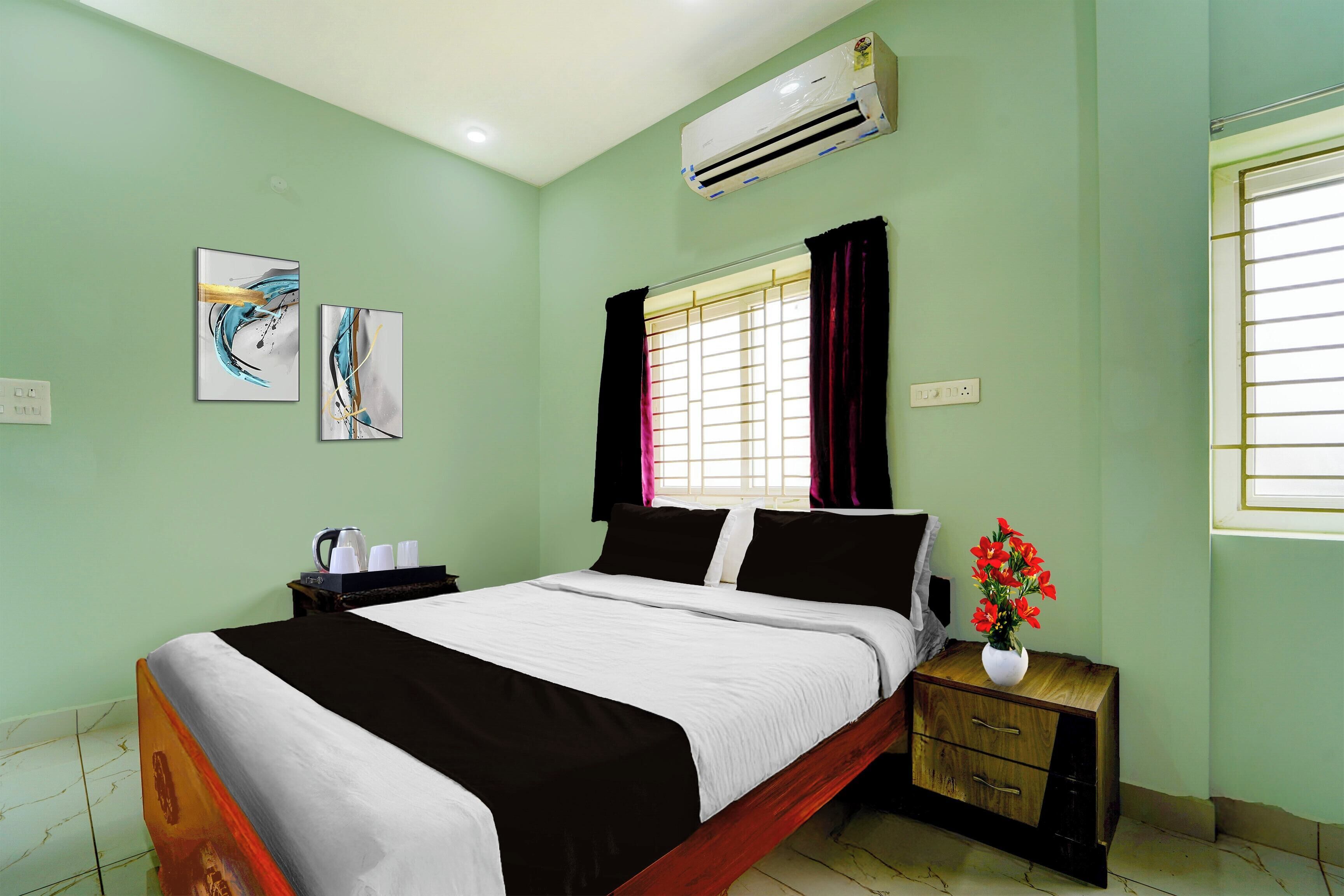 A bedroom with a bed, a nightstand, a vase with flowers, and two abstract paintings on the wall.