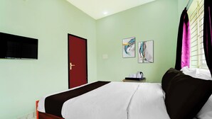 A hotel room with a bed, a television mounted on the wall, a door, and two paintings on the wall. - Collection O Thanjavur New Bus Terminal (Thanjavur)