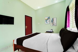 Habitación de hotel con cama, televisor montado en la pared, puerta y dos cuadros.