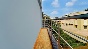 A balcony with a wooden floor, metal railing, and a view of buildings and greenery. - Collection O Thanjavur New Bus Terminal (Thanjavur)