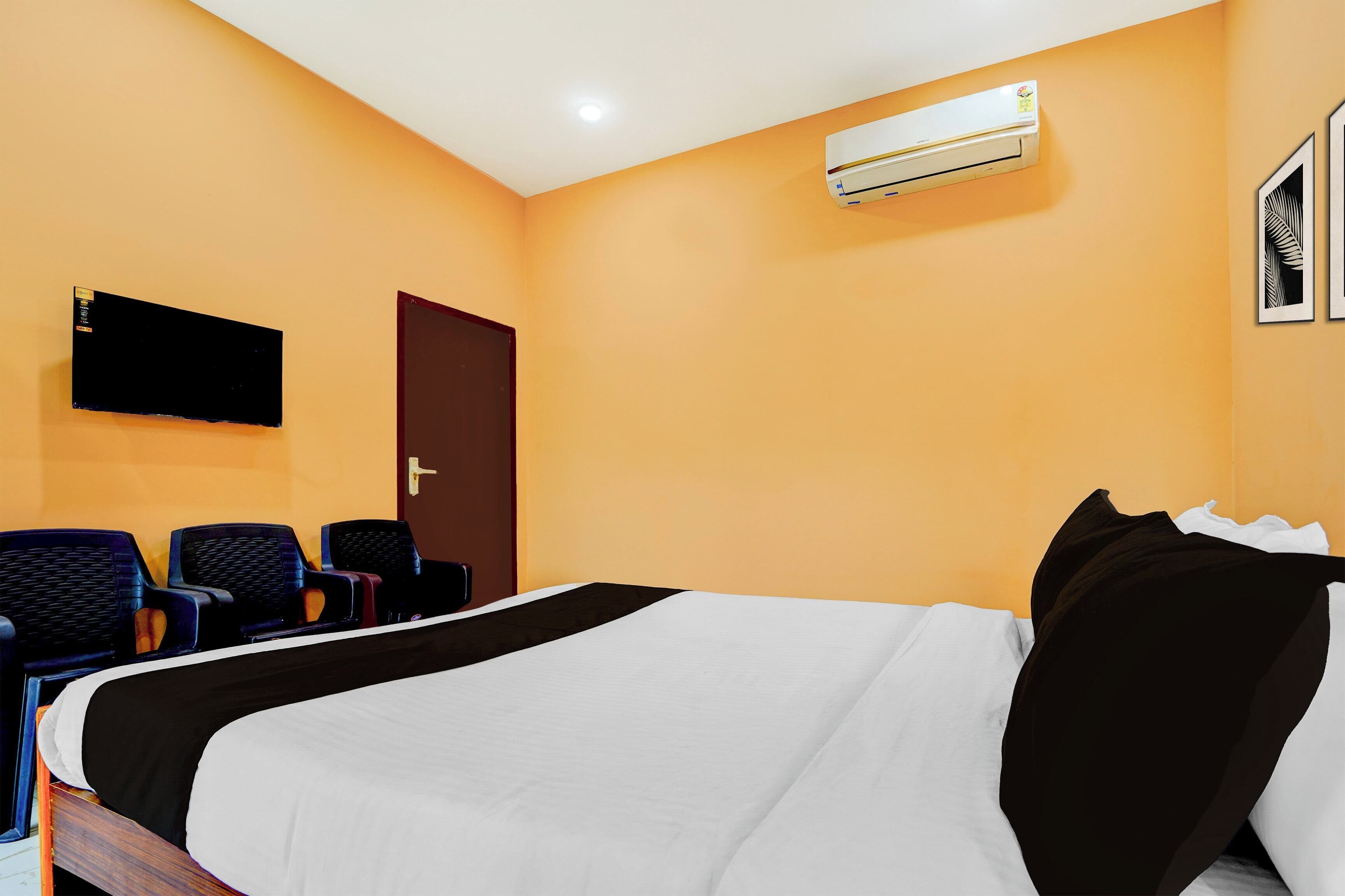 A hotel room with a bed, a flat-screen TV mounted on the wall, a door, and a seating area with chairs.