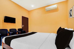 A hotel room with a bed, a flat-screen TV mounted on the wall, a door, and a seating area with chairs. - Collection O Thanjavur New Bus Terminal (Thanjavur)