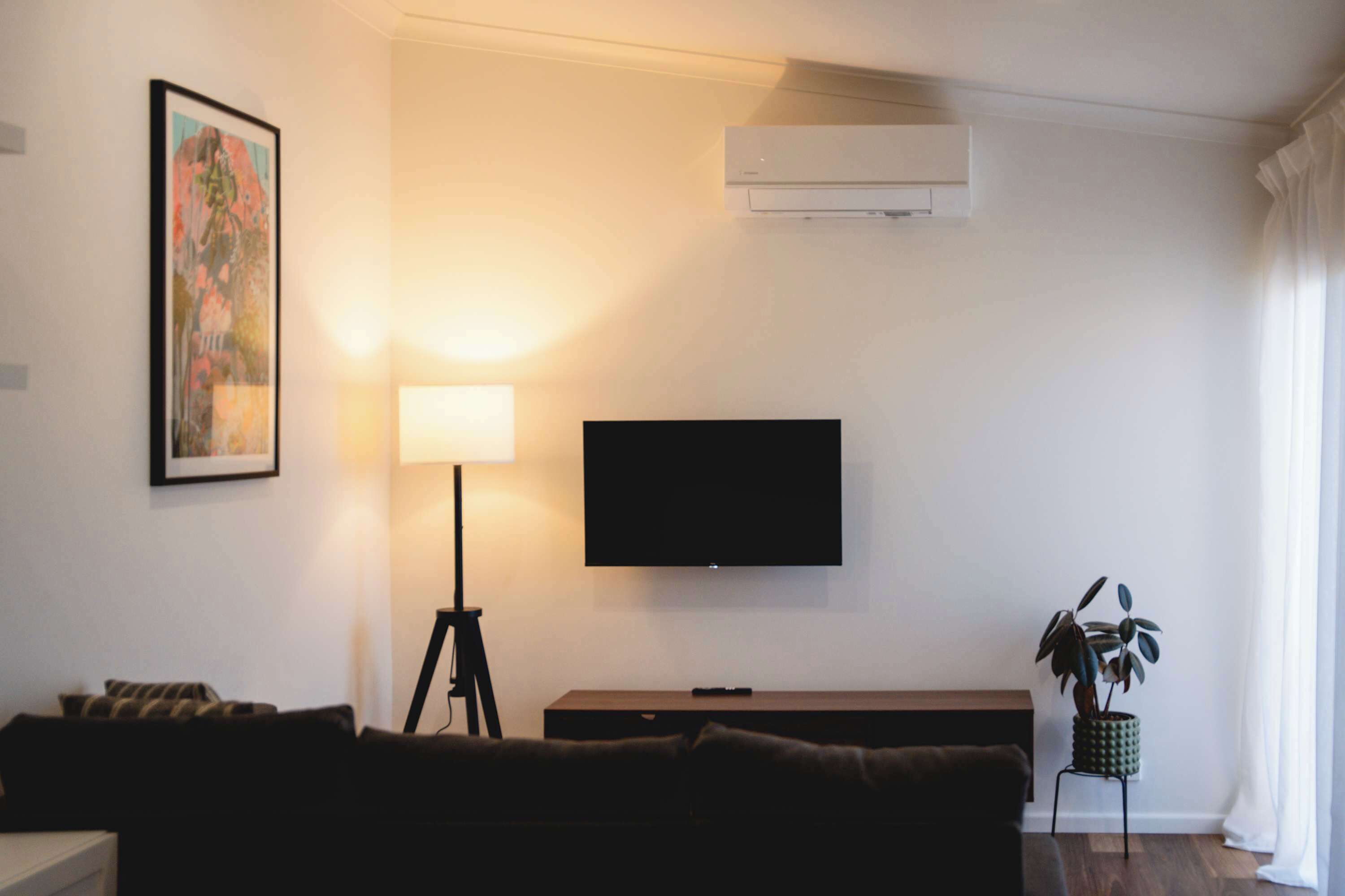 Een woonkamer met een bank, een vloerlamp, een flatscreen televisie en een schilderij aan de muur.