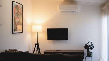 Een woonkamer met een bank, een vloerlamp, een flatscreen televisie en een schilderij aan de muur.