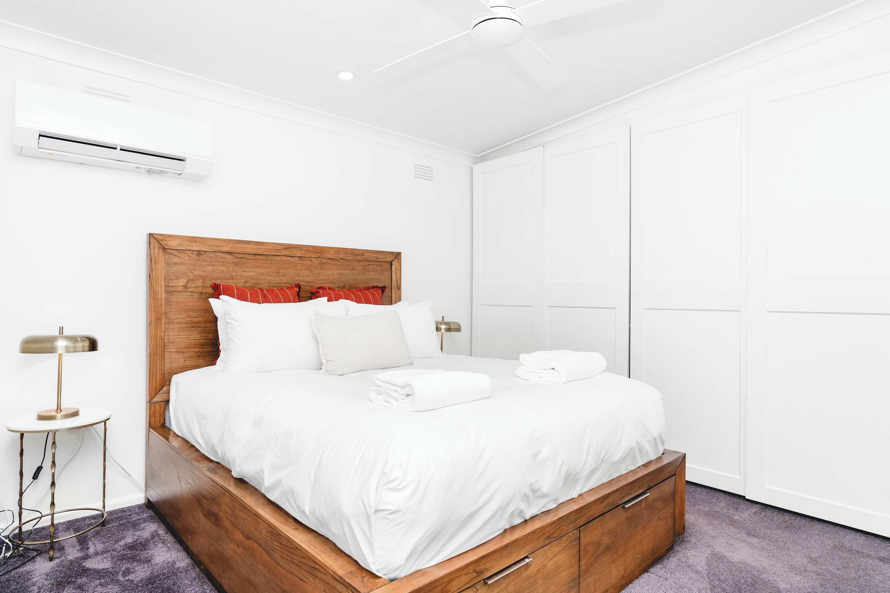Een slaapkamer met een houten hoofdeinde, wit beddengoed, een nachtkastje met een lamp en een kledingkast.