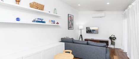 A modern living room with a grey sofa, a wooden table, and a bookshelf with various items.