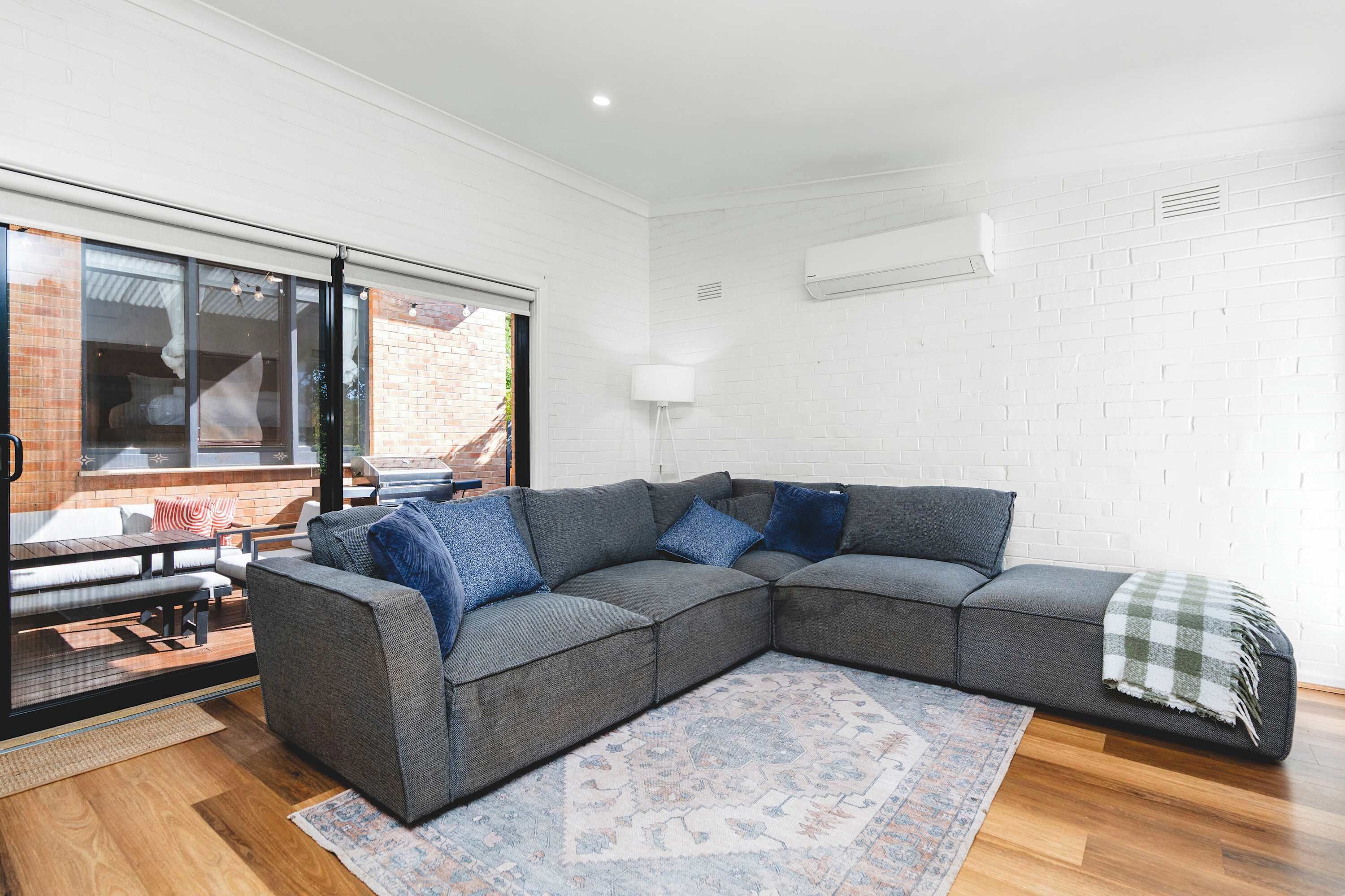A modern living room with a sectional sofa, a patterned rug, and a view of a brick exterior through large windows.