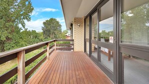 A wooden deck with a glass door leading to a room with a brick wall and a window.