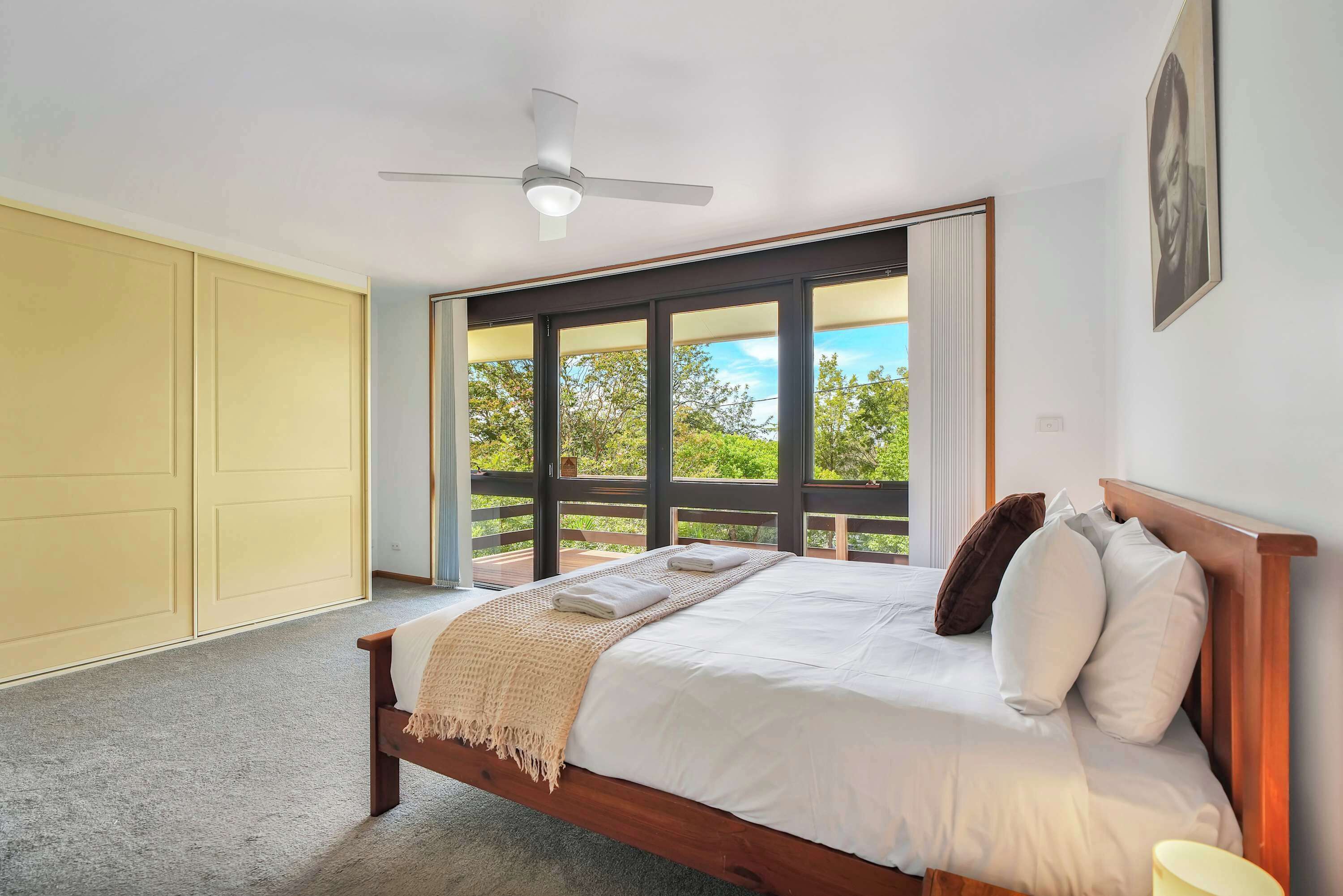 A bedroom with a bed, a ceiling fan, and a large window with a view of greenery.