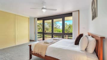 A bedroom with a bed, a ceiling fan, and a large window with a view of greenery.