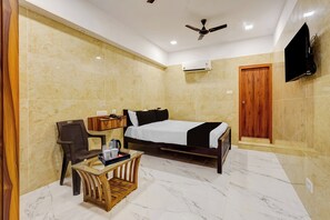Habitación de hotel con cama, escritorio con silla, televisor montado en la pared y ventilador de techo.