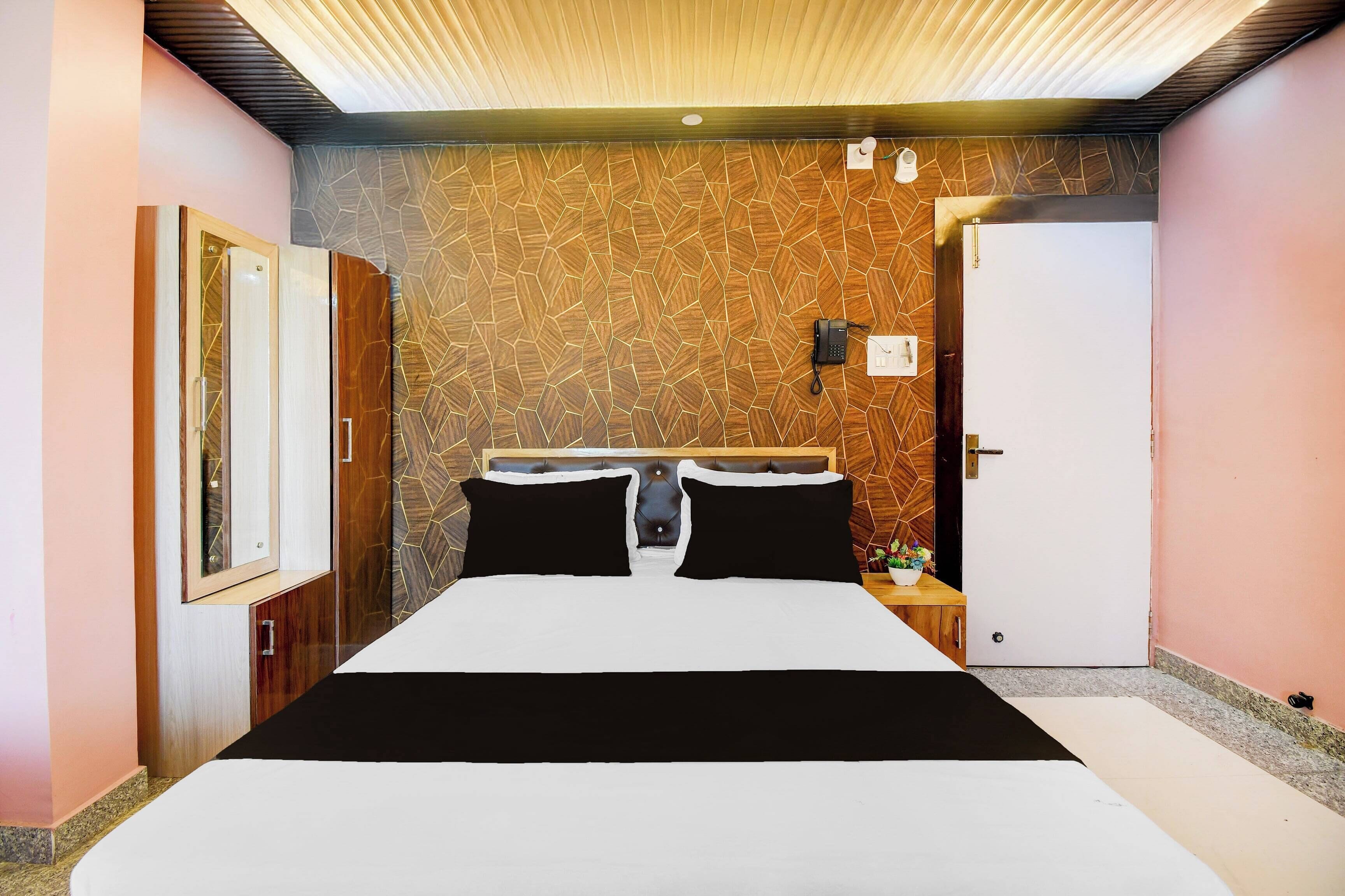 A hotel room with a bed, a bedside table, a telephone, and a door.