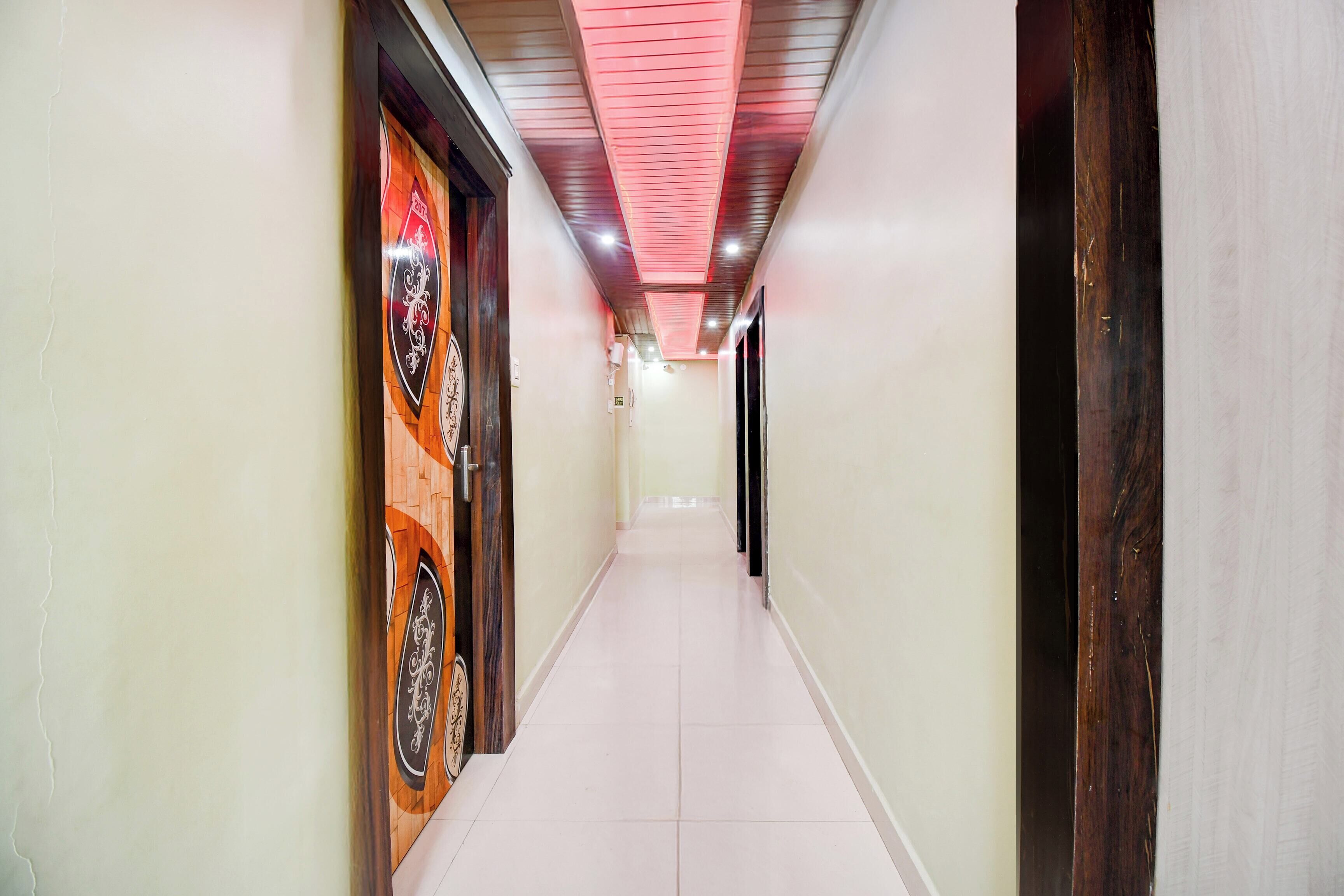 A corridor with a tiled floor, wooden doors with decorative glass panels, and a ceiling with red lighting.