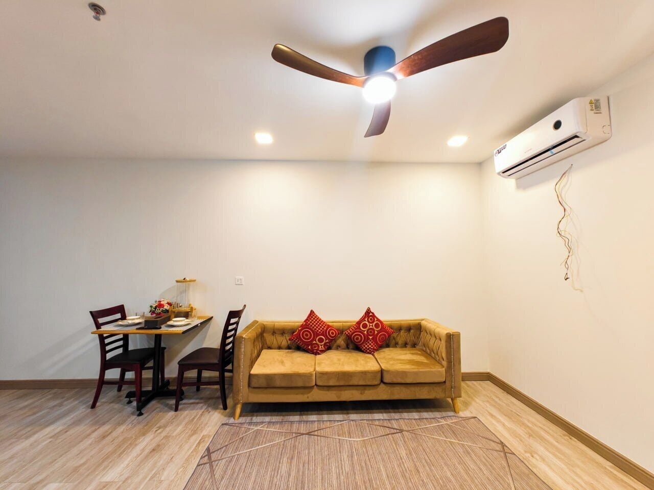 A room with a ceiling fan, an air conditioning unit, a dining table with chairs, and a sofa with decorative pillows.