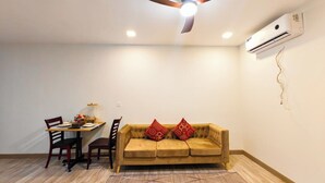 Una habitación con ventilador de techo, aire acondicionado, una mesa de comedor con sillas y un sofá con cojines decorativos.
