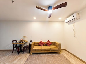 A room with a ceiling fan, an air conditioning unit, a dining table with chairs, and a sofa with decorative pillows. - Tiffany House Residence (Krong Siem Reap)
