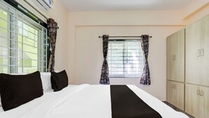 A hotel room with a bed, two windows with curtains, a wardrobe, and an air conditioning unit. - Collection O Tirupati Railway (Tirupati)