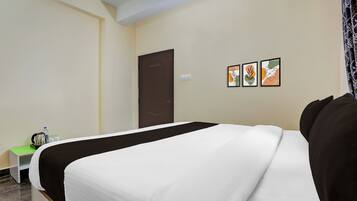 Habitación de hotel con una cama, una mesita con hervidor y tazas, y una puerta. Hay tres cuadros enmarcados en la pared.
