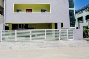 A two-story building with a flat roof, a balcony on the upper floor, and a gated entrance.