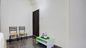 A hallway with two chairs, a door, and a small table with a kettle and water bottle. - Collection O Tirupati Railway (Tirupati)