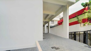 A corridor with a tiled floor, a white wall, and a red and green building in the background.