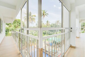 A spacious balcony with a view of palm trees and a swimming pool. - Collection O Valiyavila Junction (Thiruvananthapuram)