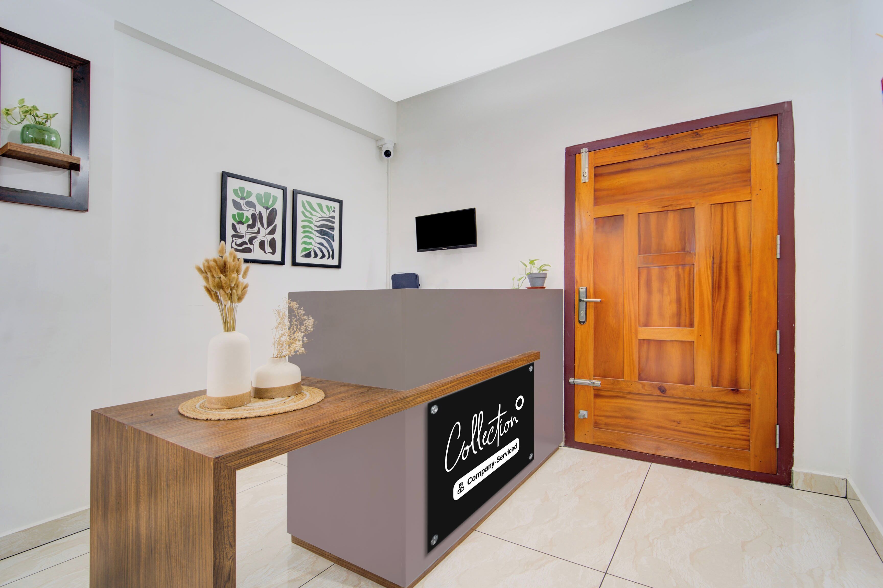 A reception desk with a sign indicating it's company-serviced, a wooden door, and two framed botanical prints on the wall.