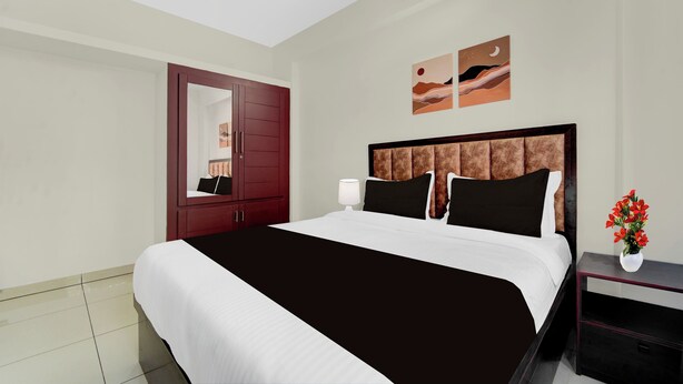 A hotel room with a large bed, a nightstand with a lamp, a red wardrobe, and two wall art pieces.