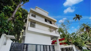 A multi-story building with balconies, a gated entrance, and lush greenery around.