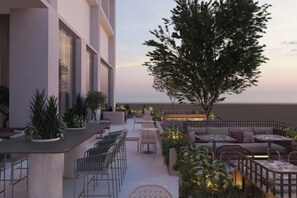 An outdoor seating area with tables and chairs, surrounded by plants and a large tree. - AC Hotels by Marriott Airport City Belgrade (Belgrade)