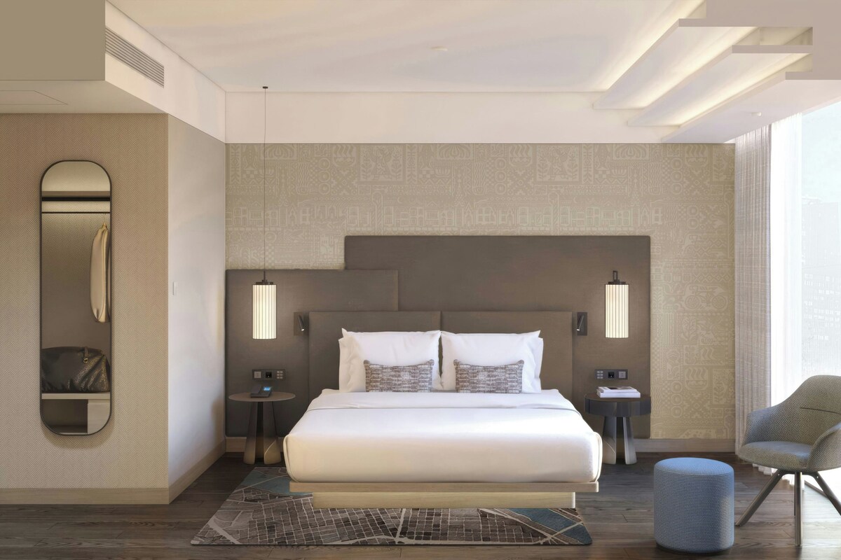 A modern hotel room with a large bed, bedside tables, a mirror, and a chair.