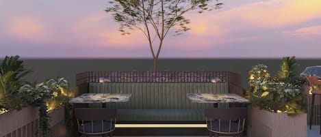 An outdoor seating area with two tables and chairs, a wooden fence, and a tree.