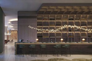 A bar area with a long counter, multiple shelves of bottles, and hanging lights. - AC Hotels by Marriott Airport City Belgrade (Belgrade)